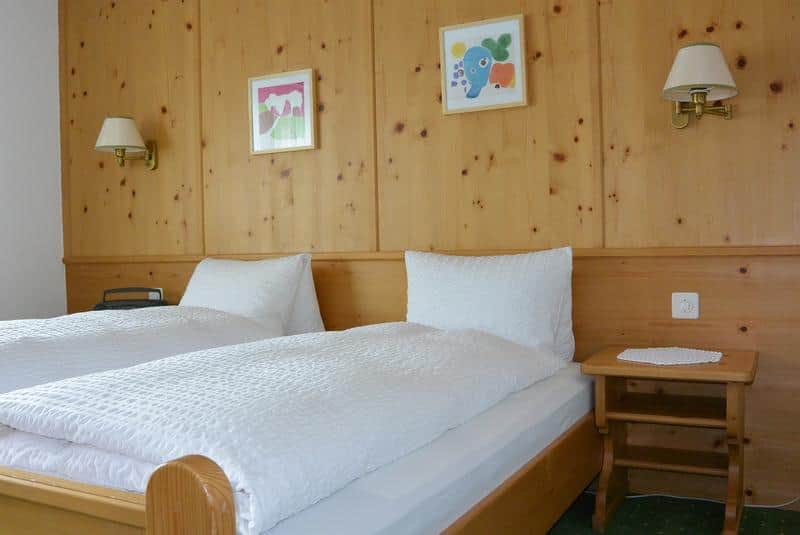 Blick Doppelbett mit Holzrahmen beidseitig ein Nachttisch, Rückwand aus Holz mit je einer Leuchte und 2 Bildern